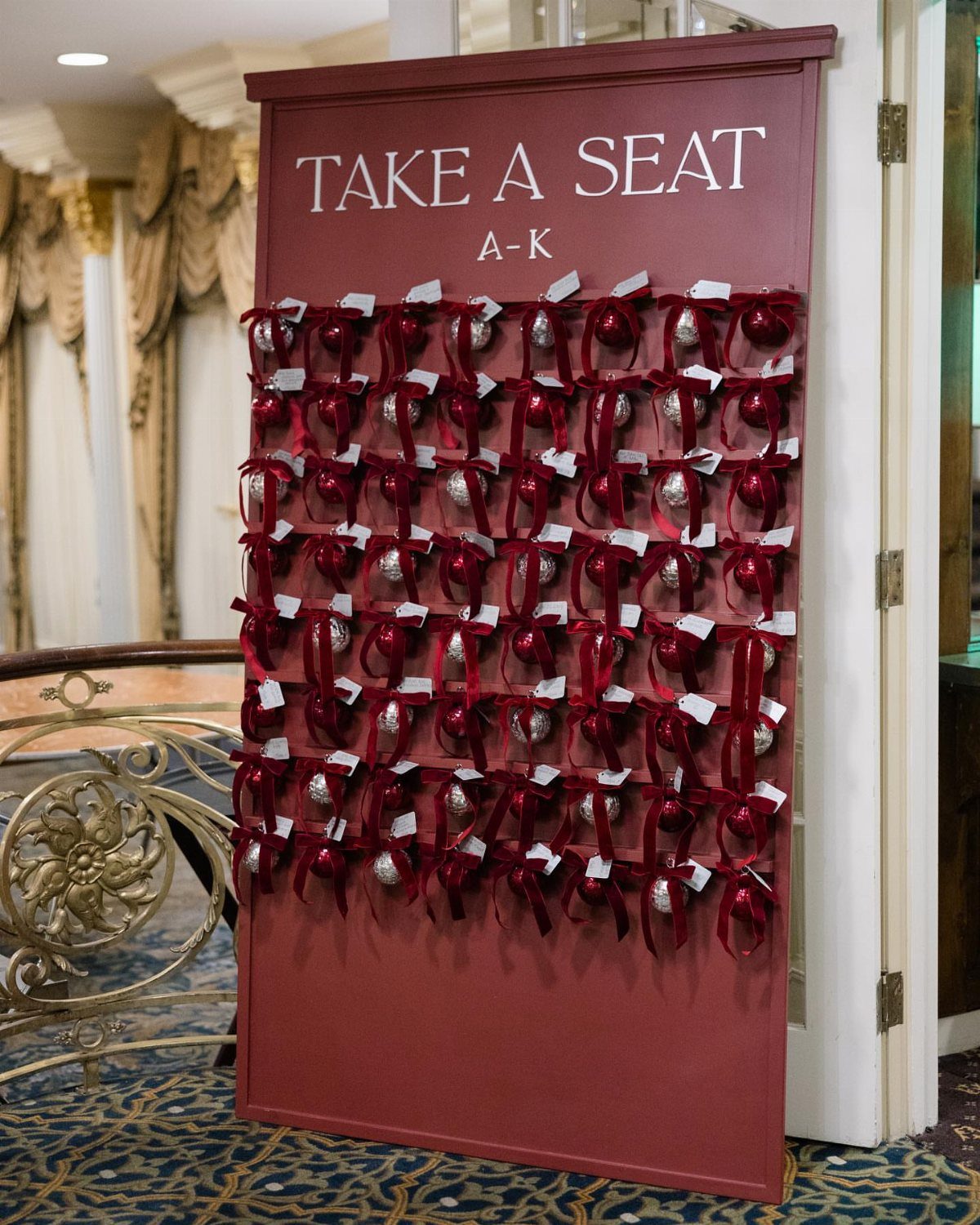 Red seating chart board with white name tags and silver ornaments for guests