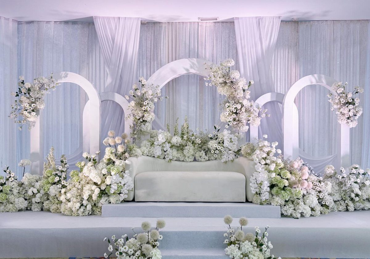 White wedding stage with a sofa, floral arrangements, and arched backdrops.