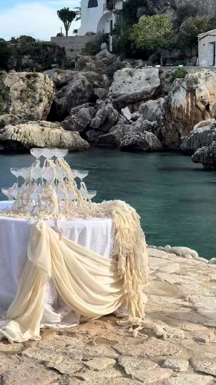 Champagne tower of stacked glasses on a draped table by a rocky coast