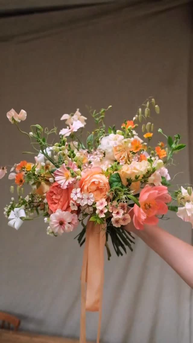 Peach and orange wedding bouquet with greenery held against a beige background