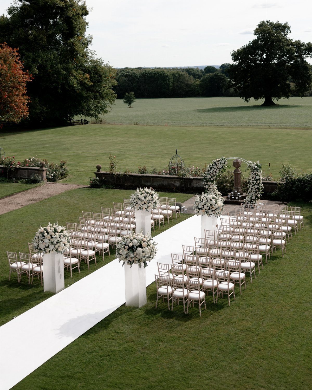 Outdoor wedding ceremony setup with white chairs and floral arrangements on a green lawn