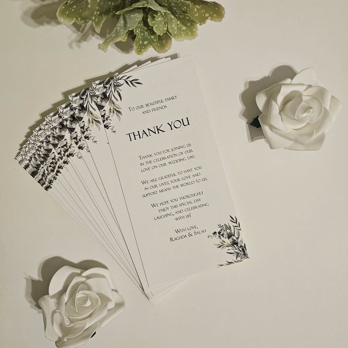 Wedding thank you cards with floral designs surrounded by white roses and a succulent.