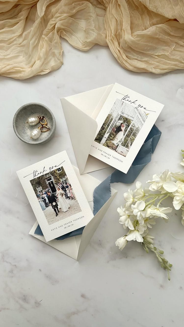 Wedding thank you cards with couple photos on a marble surface with flowers.