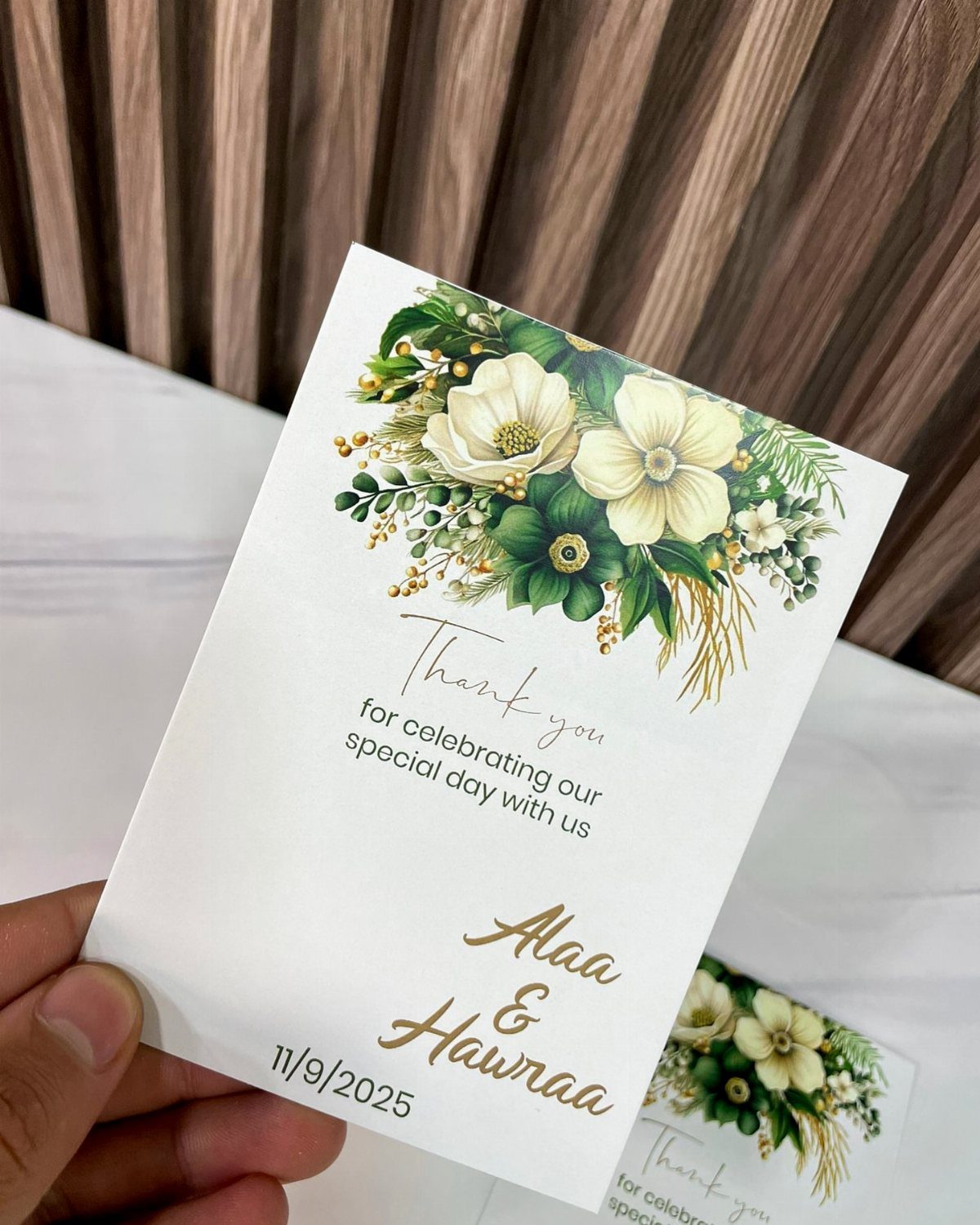 Wedding thank you card with white floral illustrations and gold cursive text.