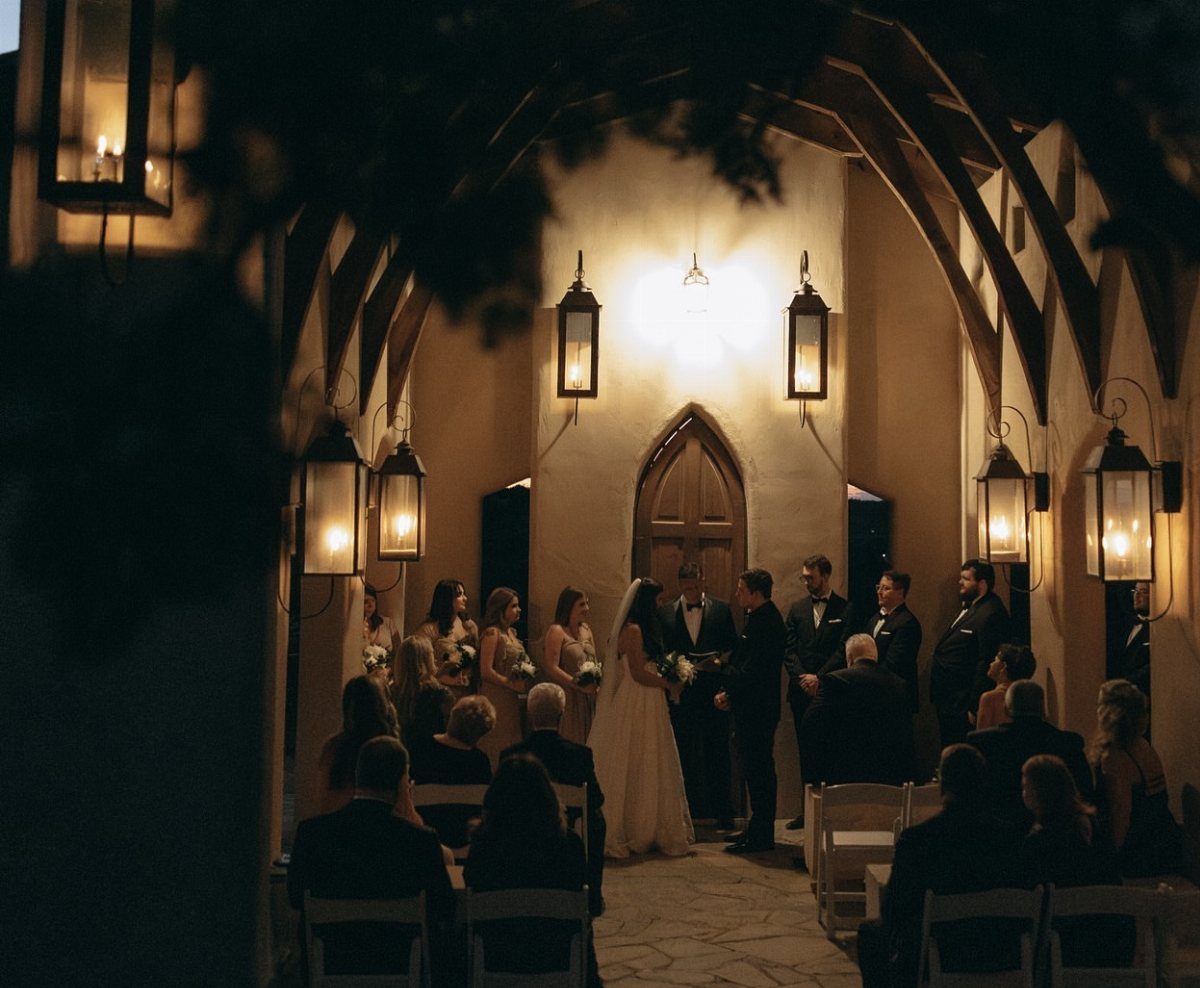 Wedding ceremony in a historic courtyard with arched ceilings and warm lantern lighting.