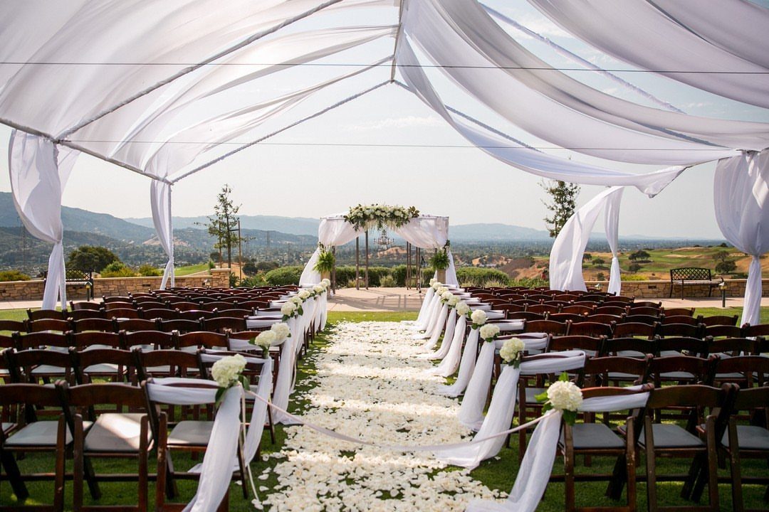 Outdoor wedding ceremony setup with white canopy, petal aisle, and scenic hill views.