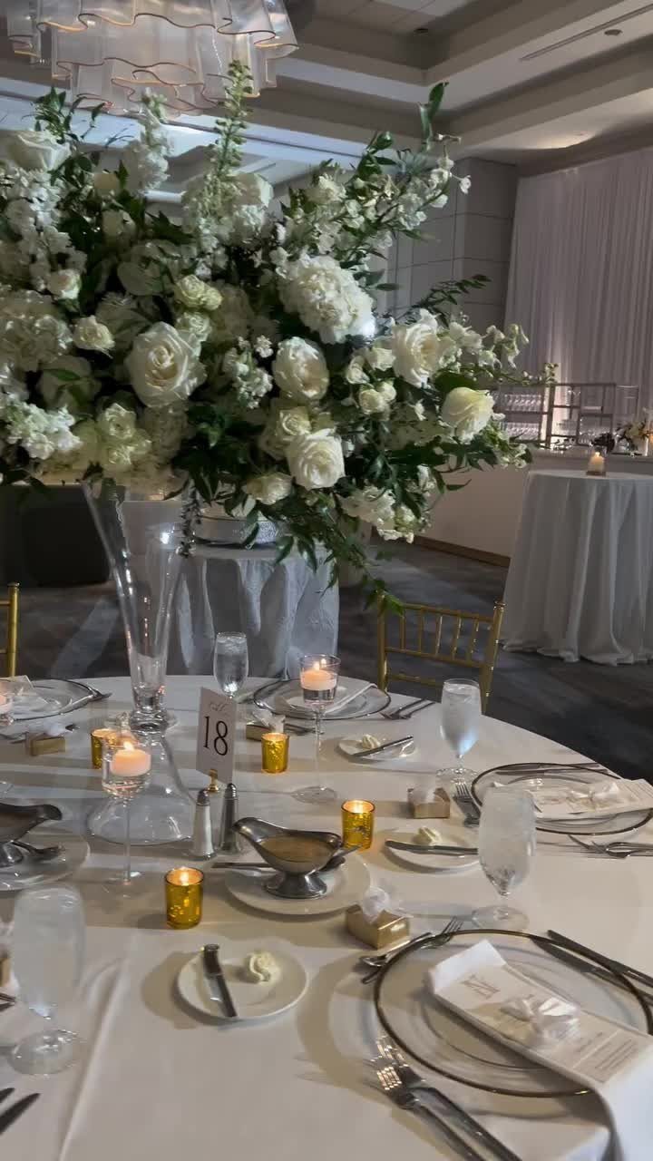 Formal wedding table setting with white roses, greenery, and gold votive candles.