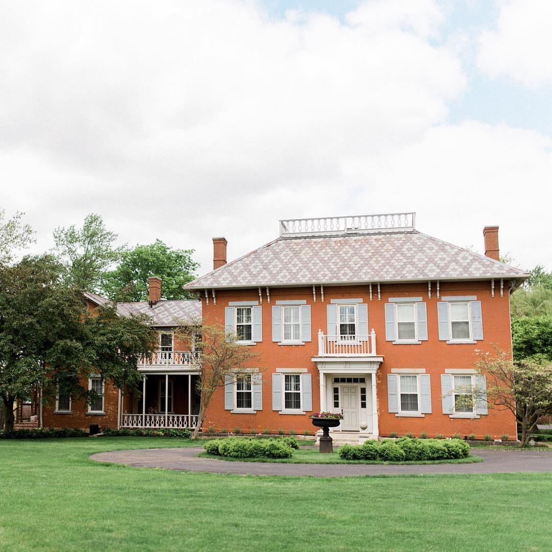 Red brick historic house with blue shutters and a white roof balustrade.