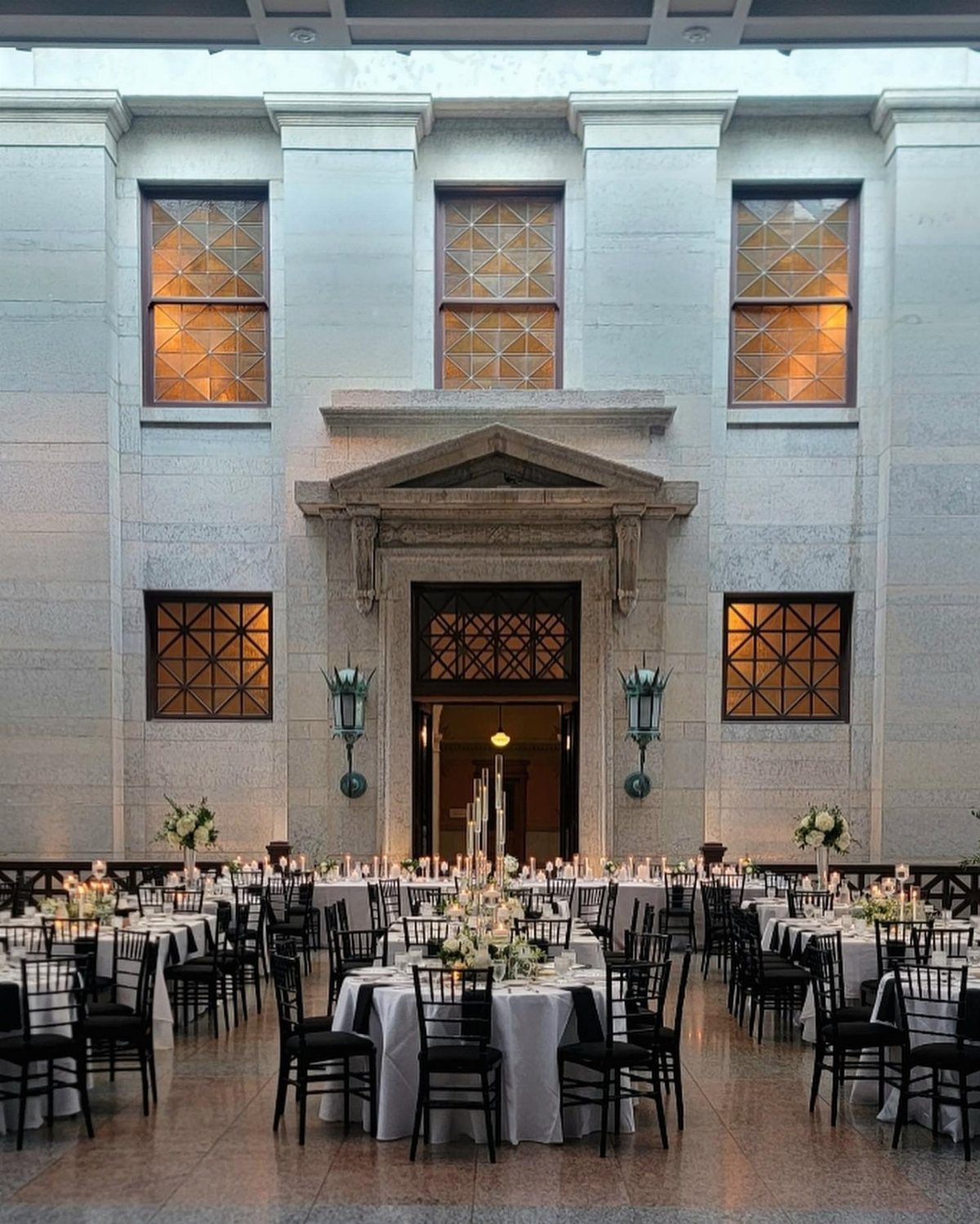 Elegant wedding reception setup with round tables and black chairs in a stone hall.