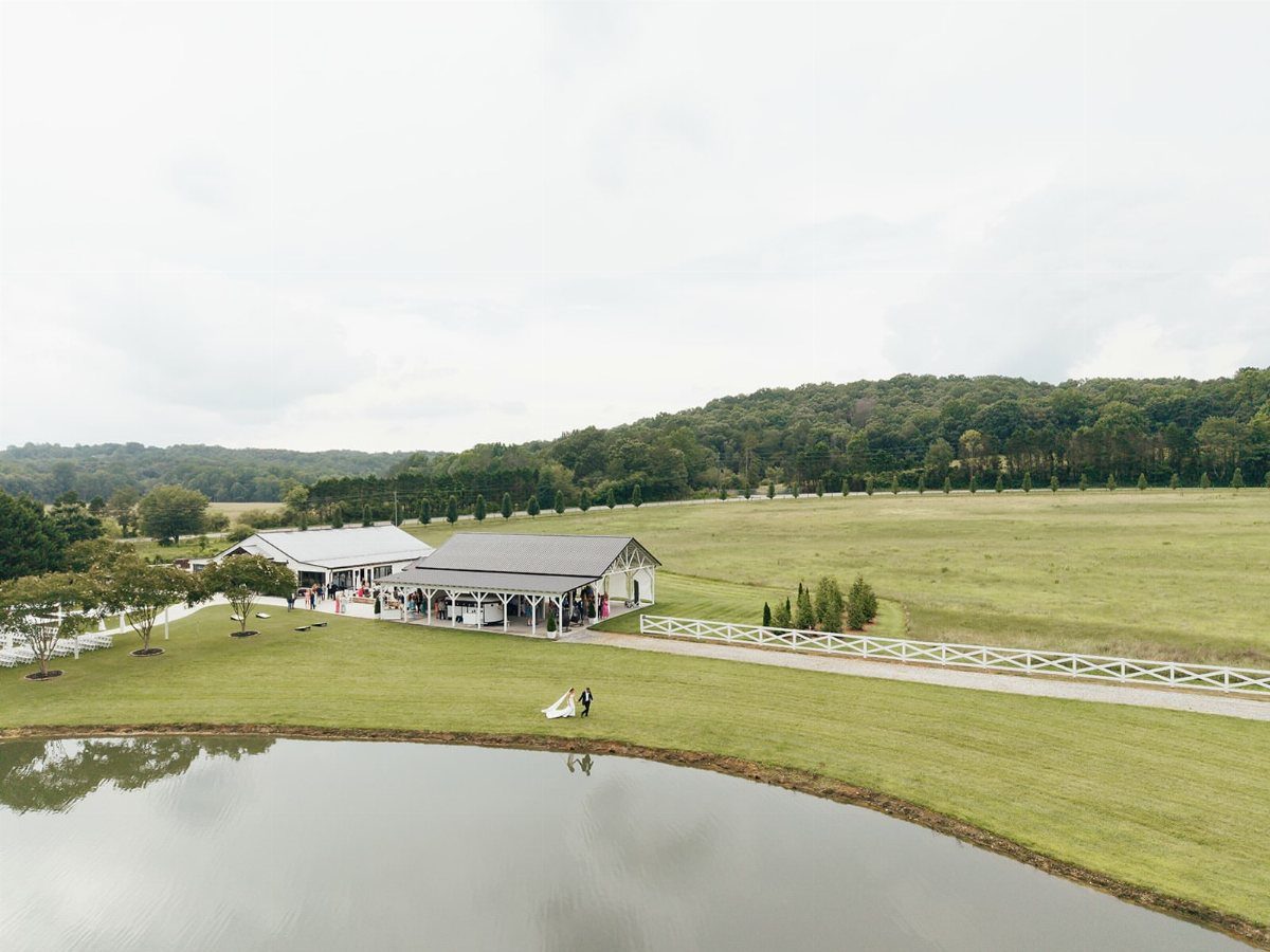White barn event venue with a pond and couple in a rural landscape
