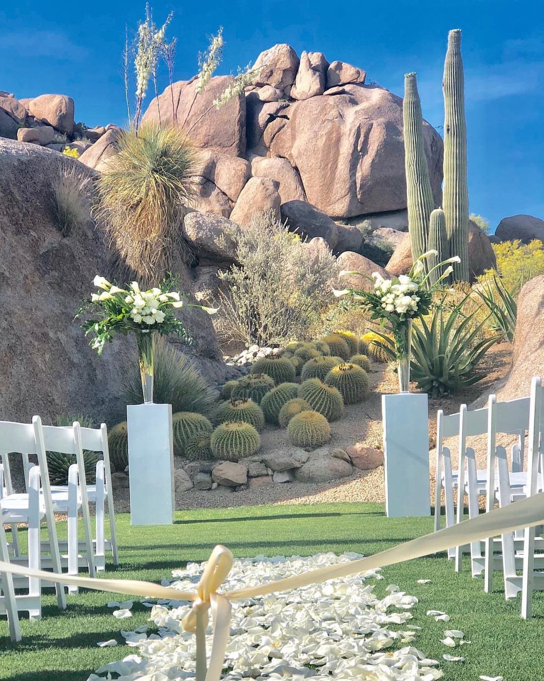 Wedding ceremony setup with white chairs and flowers against Arizona desert boulders and cacti.