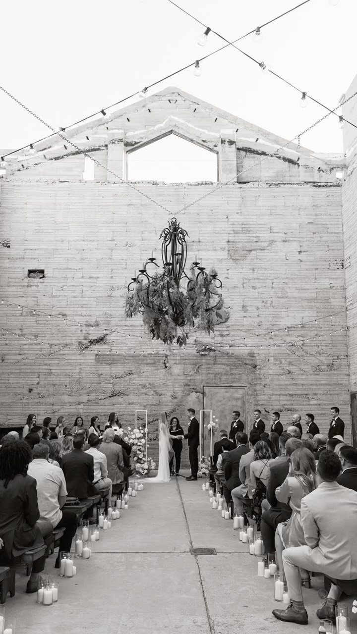 Wedding ceremony in an industrial concrete courtyard with guests and a large chandelier.