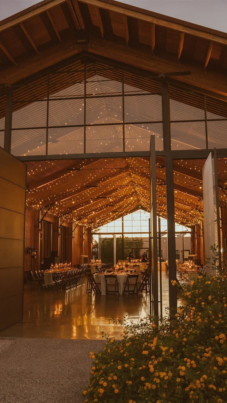 Rustic event venue with string lights, dining tables, and yellow flowers in foreground.