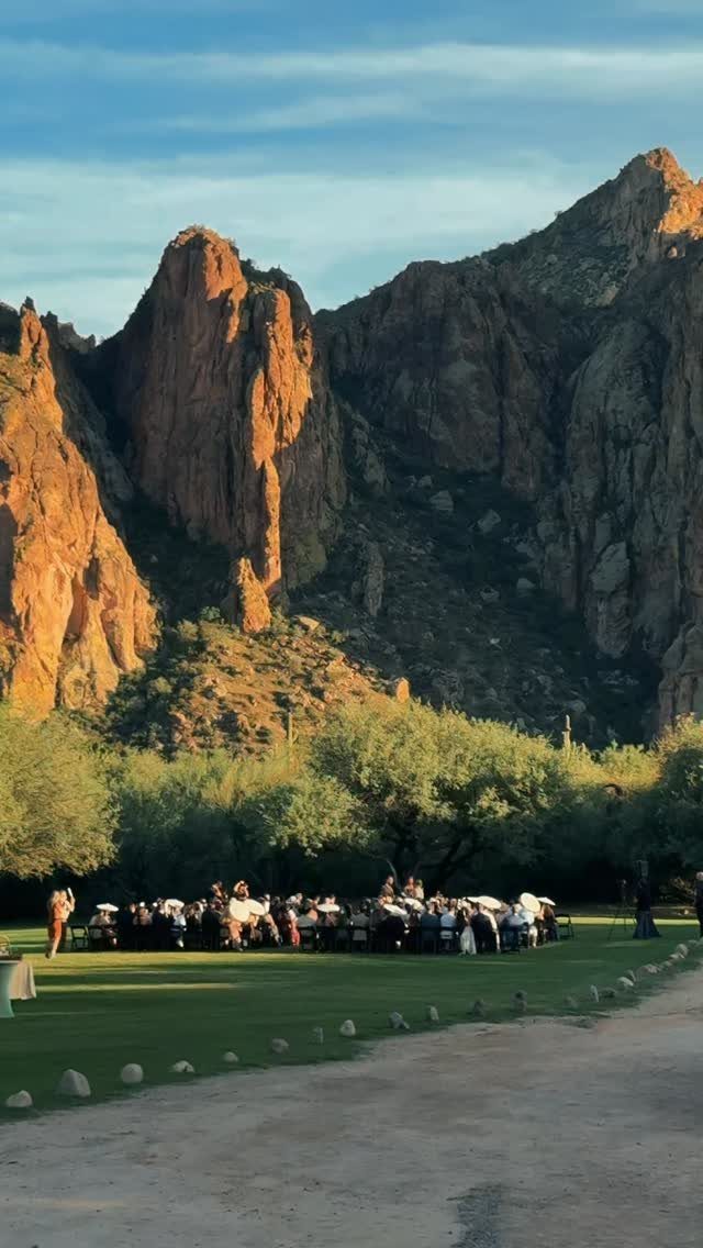 Outdoor event seating on a green lawn with towering red rock cliffs behind.