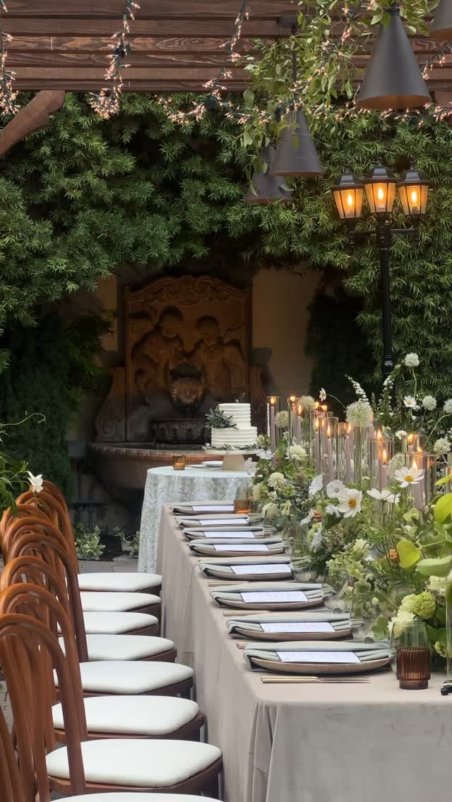 Elegant outdoor wedding table setting with white flowers and greenery under a wooden pergola.