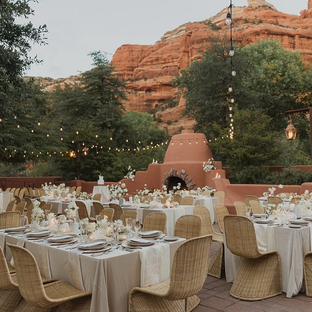 Outdoor wedding reception with white tables and wicker chairs against Sedona red rock cliffs.