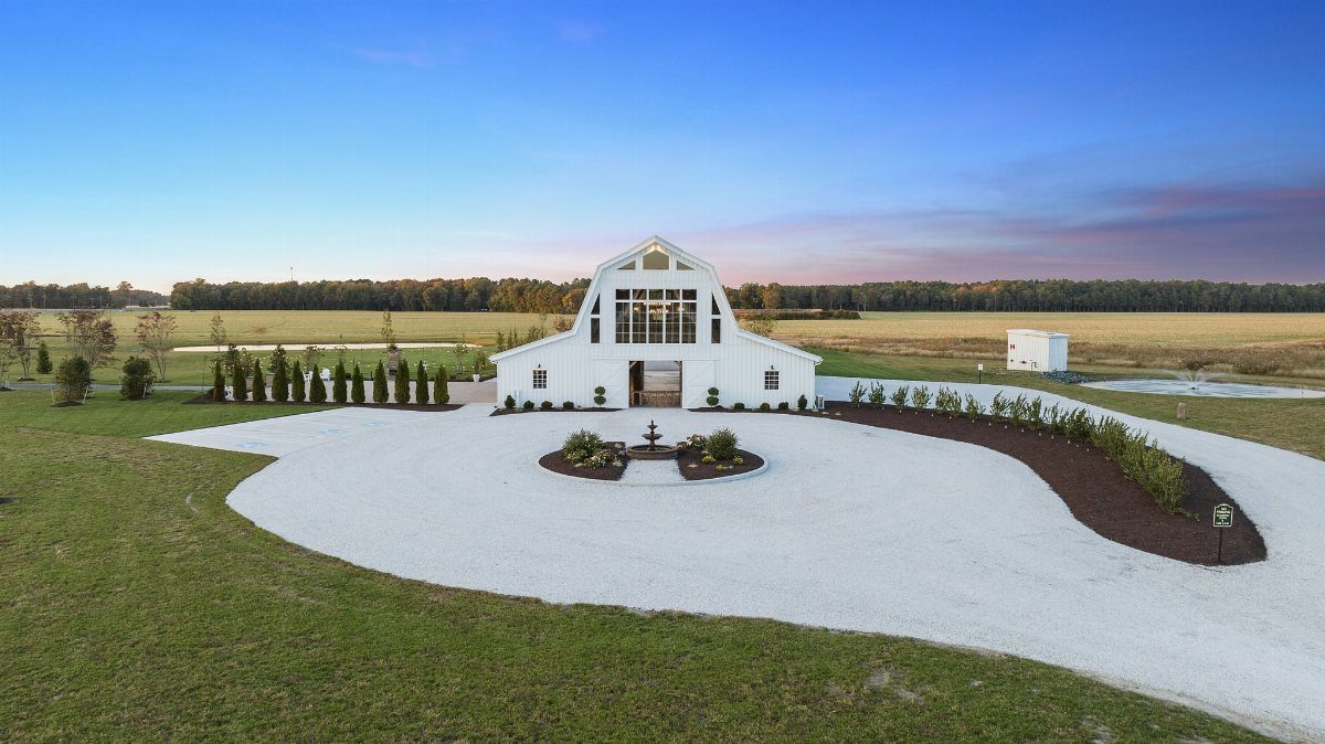 White modern barn wedding venue with a gravel driveway in a rural field.