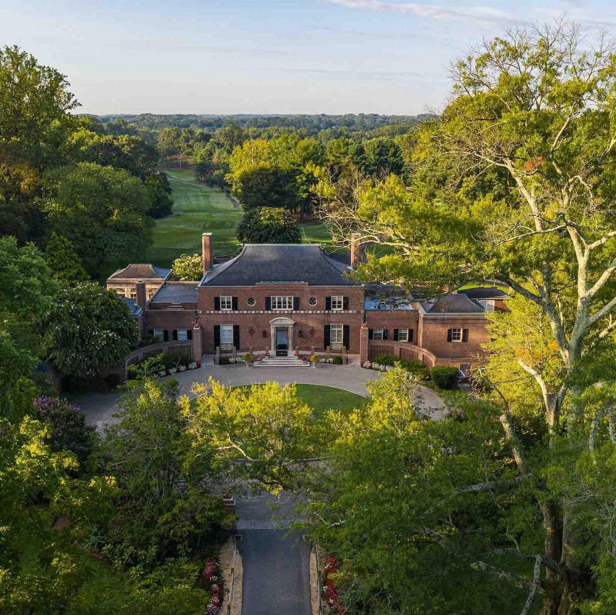 Large red brick historic manor house surrounded by green trees and lawns.