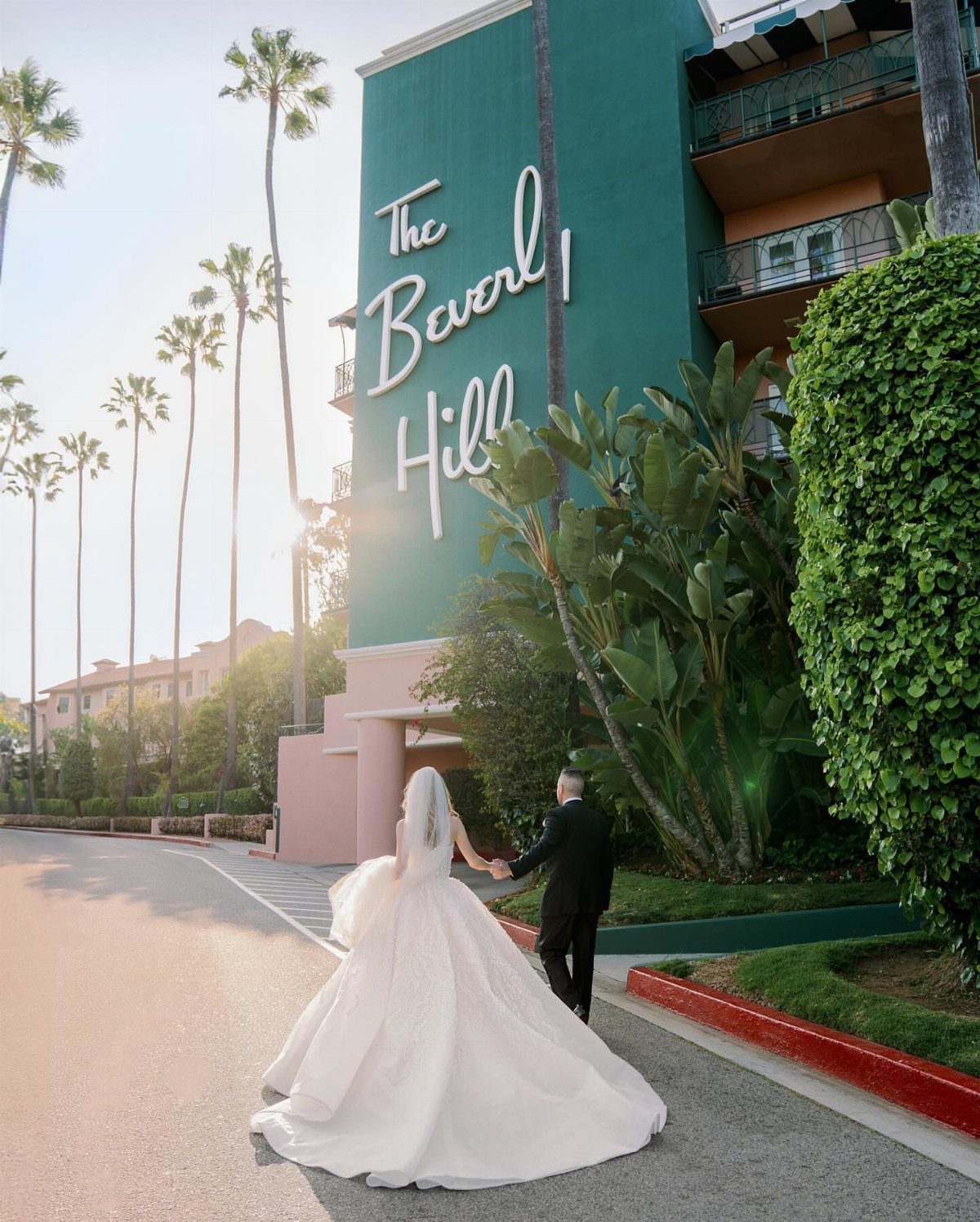 Bride and groom walking toward the iconic Beverly Hills Hotel teal exterior and signage.
