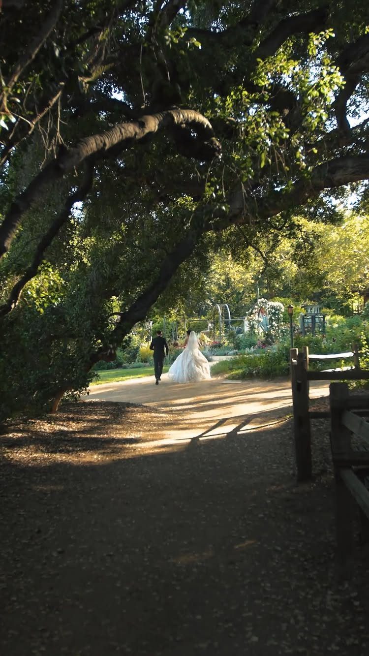 Bride and groom walking along a sunlit path in a lush garden venue.