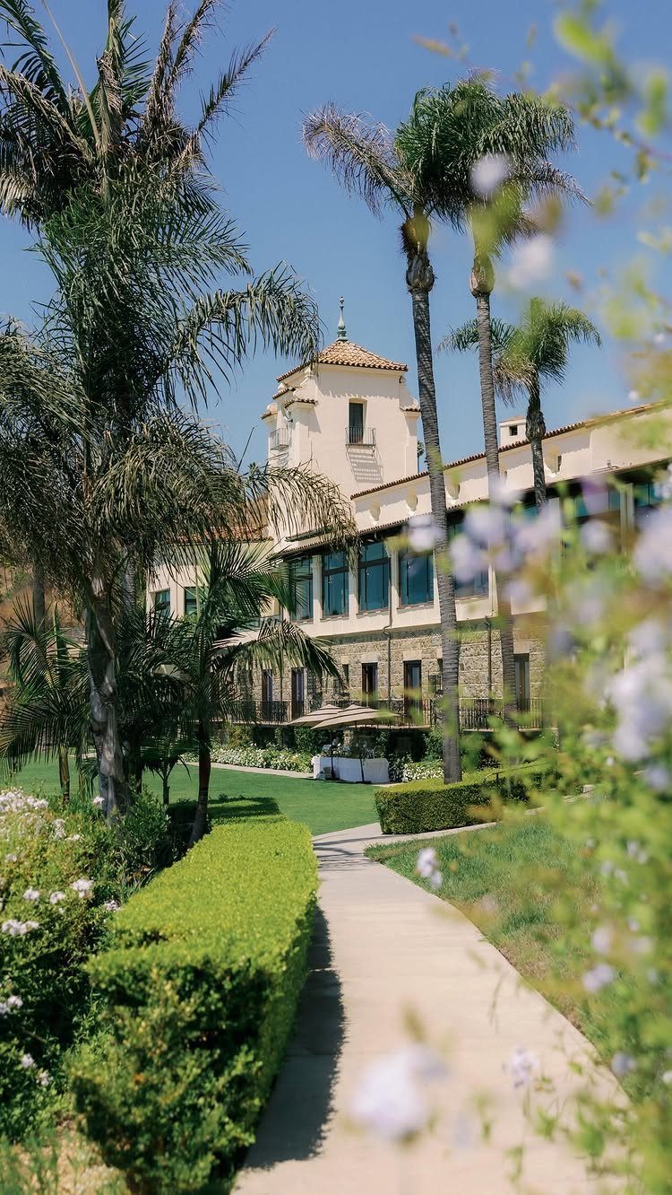 Mediterranean style building with palm trees and manicured gardens under a blue sky
