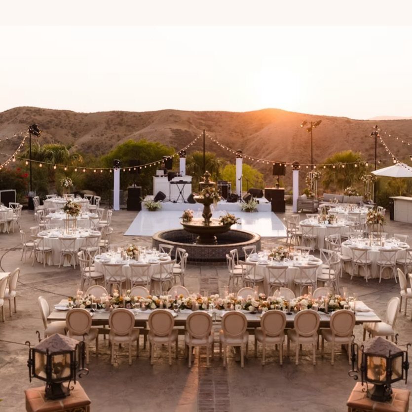 Outdoor wedding reception setup with white tables and chairs overlooking rolling brown hills.