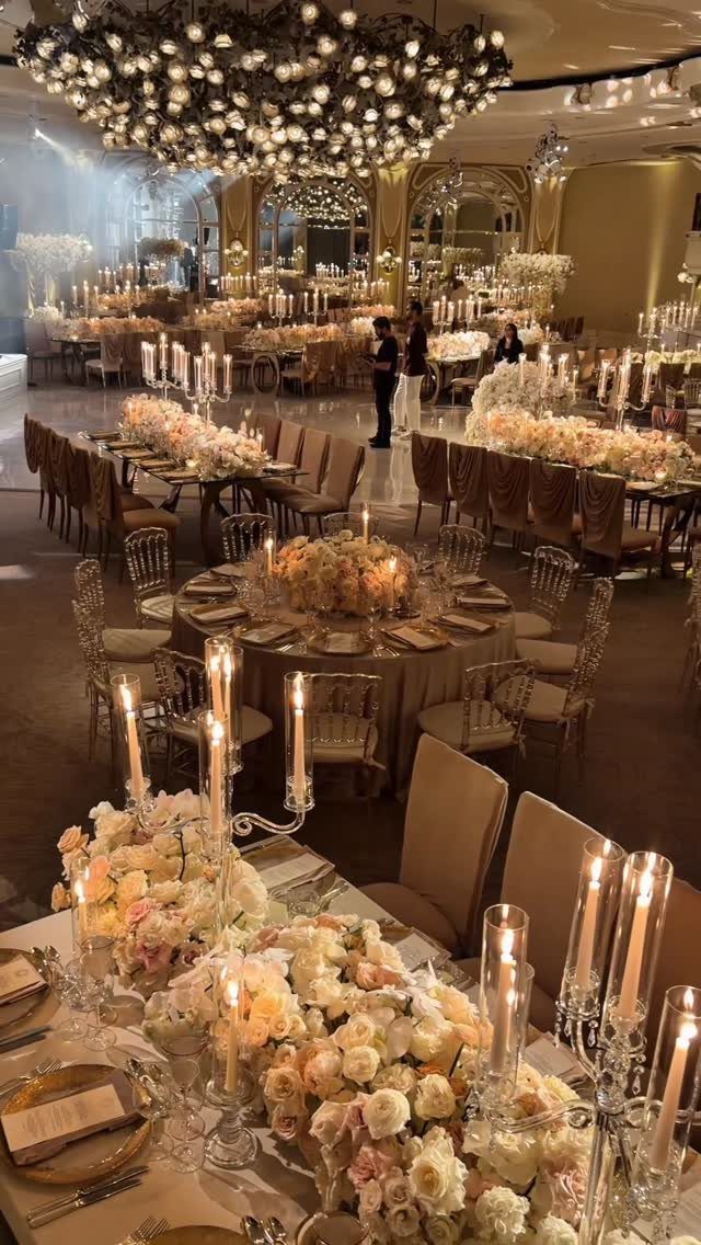 Opulent ballroom wedding reception with peach rose centerpieces, gold chairs, and crystal chandeliers.
