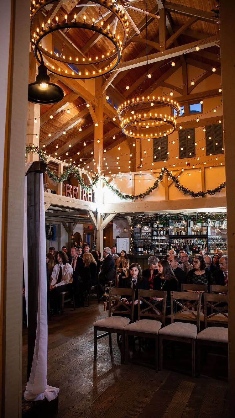 Rustic barn wedding ceremony with wooden beams, warm string lights, and seated guests.