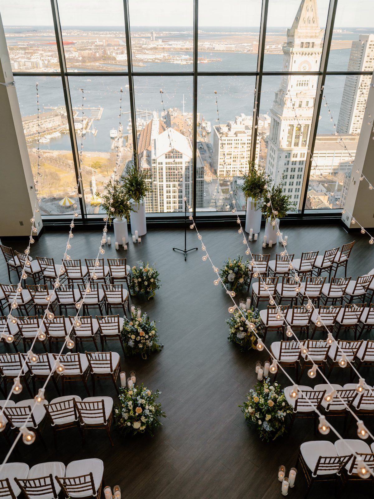 Wedding ceremony setup with white chairs and floral arrangements overlooking a city skyline.