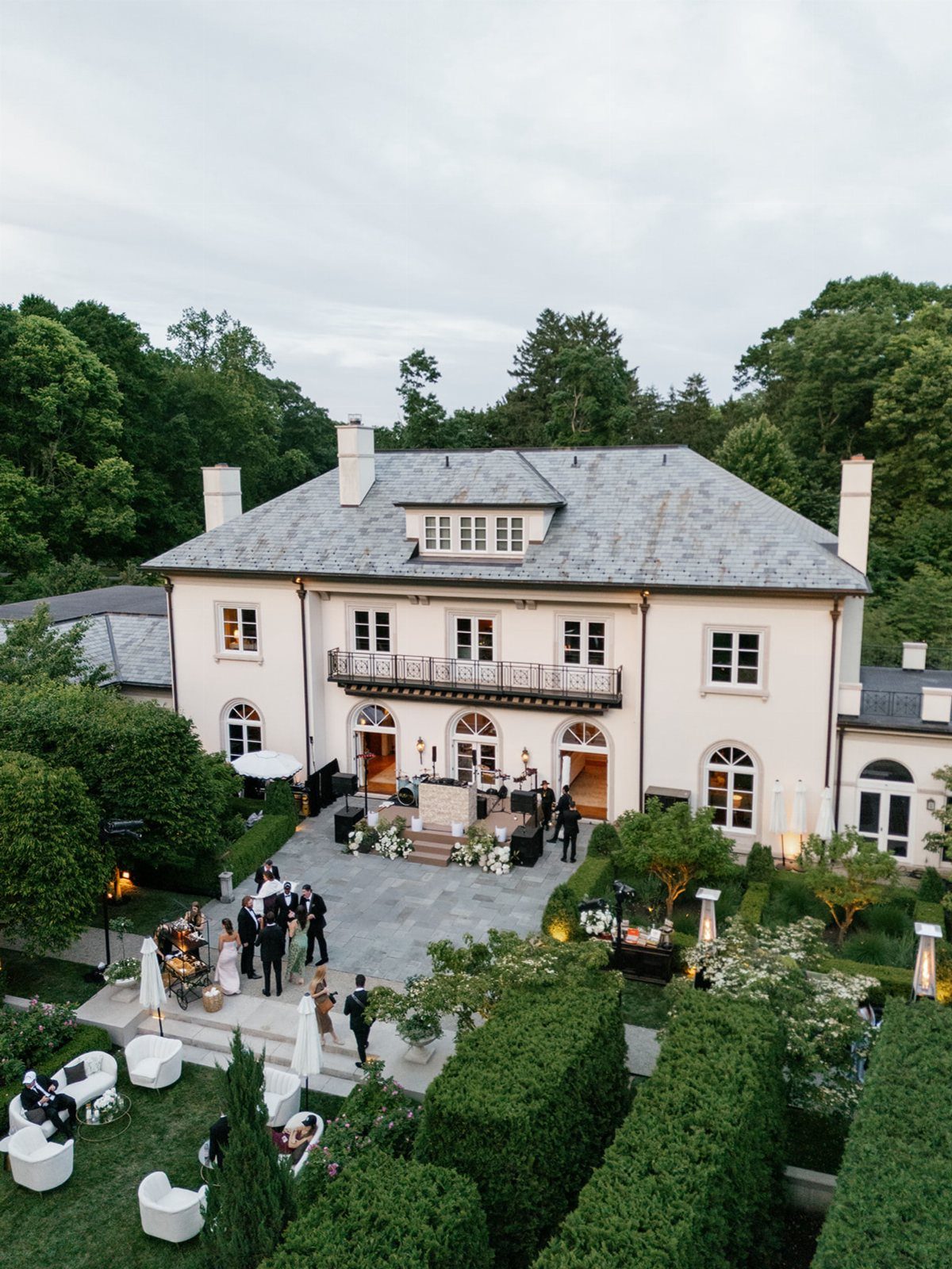 White historic mansion with guests in formal wear on a stone patio and lawn