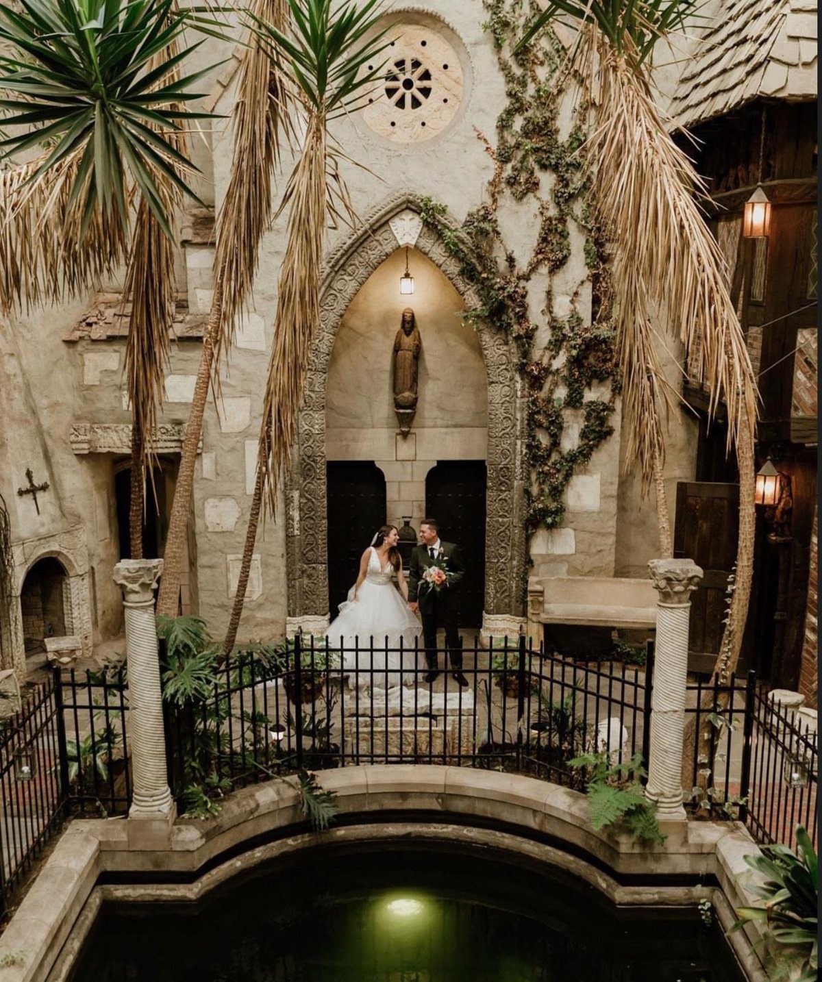 Bride and groom posing before a gothic stone archway at a castle venue.