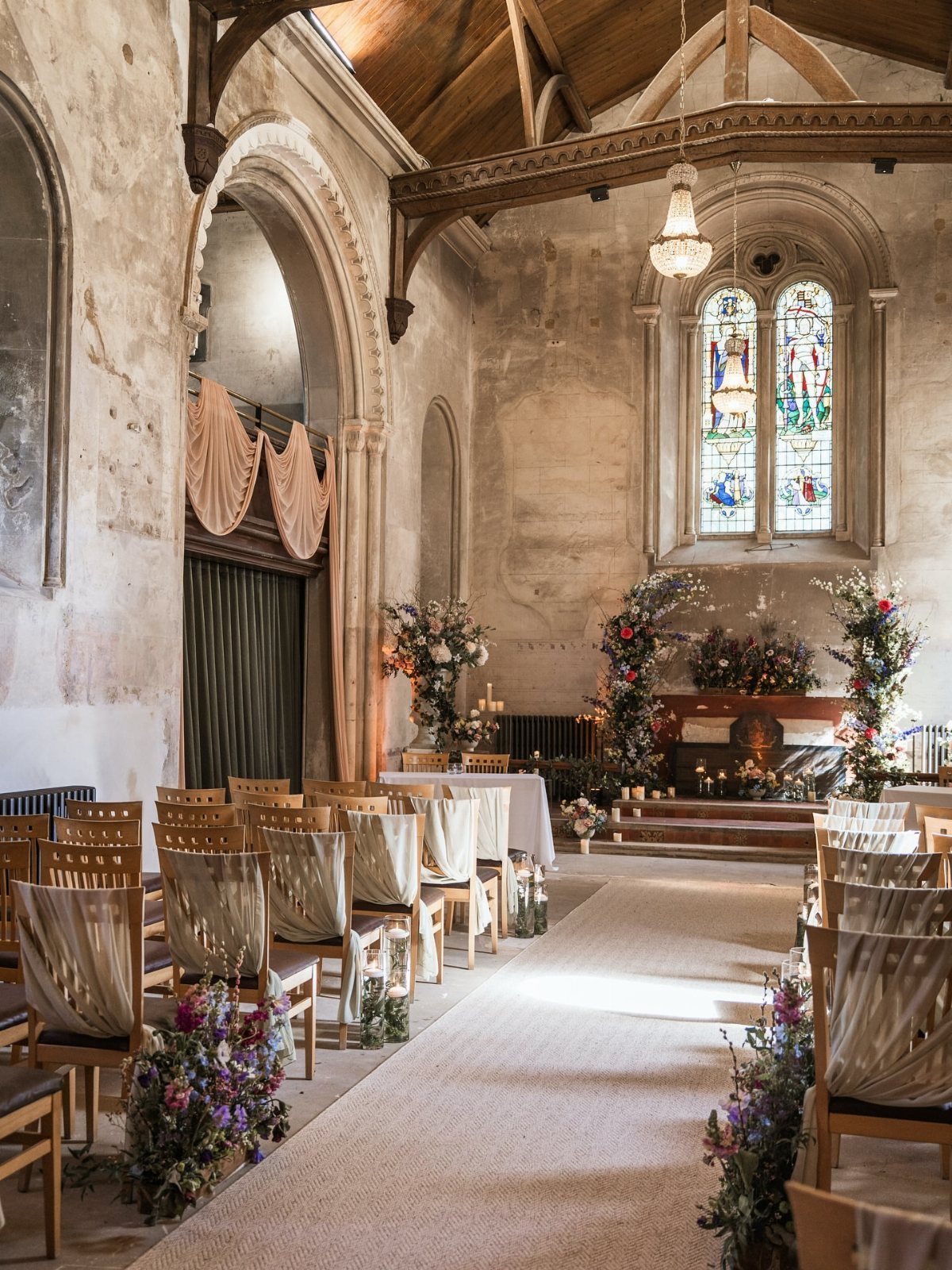 Stone chapel interior with a white aisle runner and floral arrangements for a wedding.