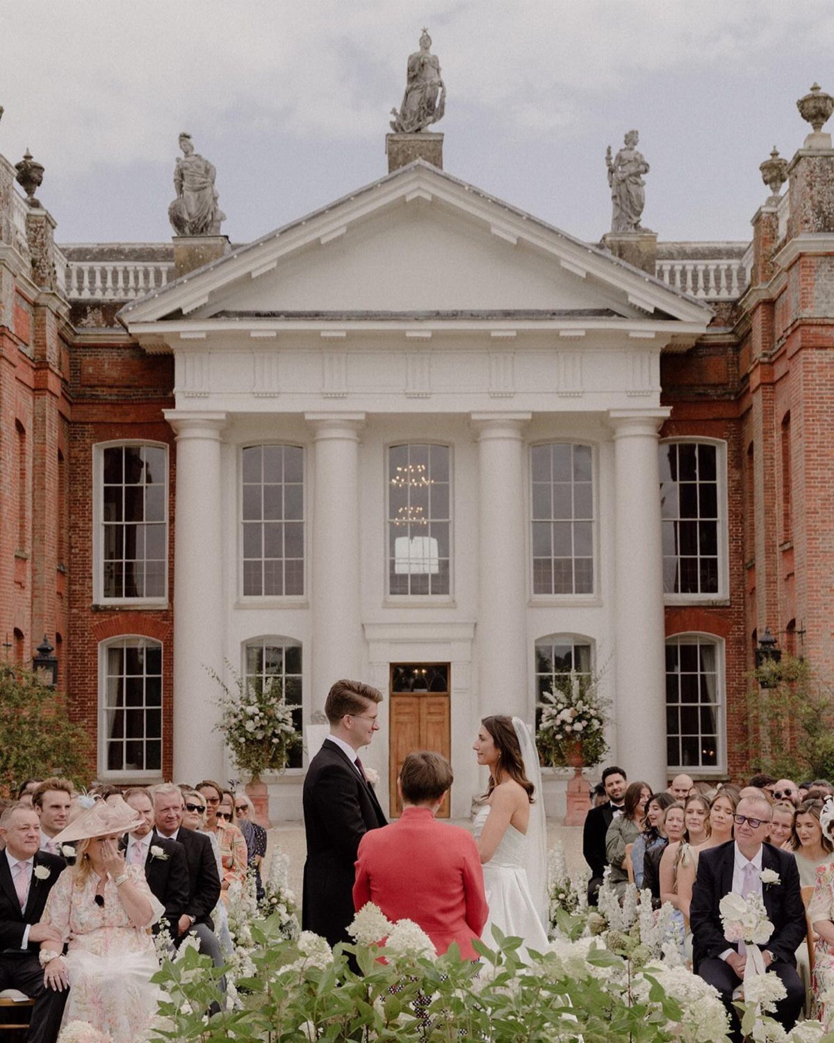 Wedding ceremony in front of a grand neoclassical building with white columns and statues.