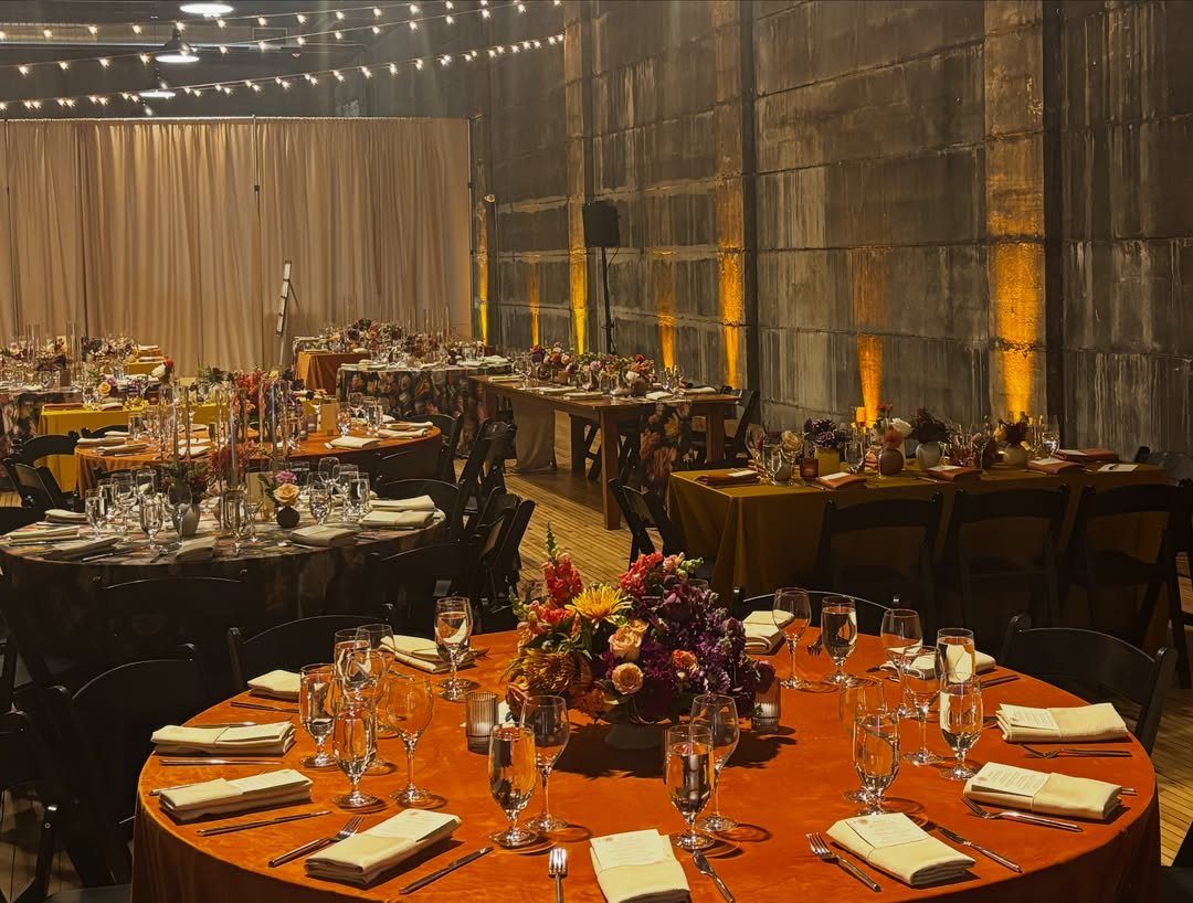 Elegant wedding reception setup with orange tablecloths and floral centerpieces in industrial venue