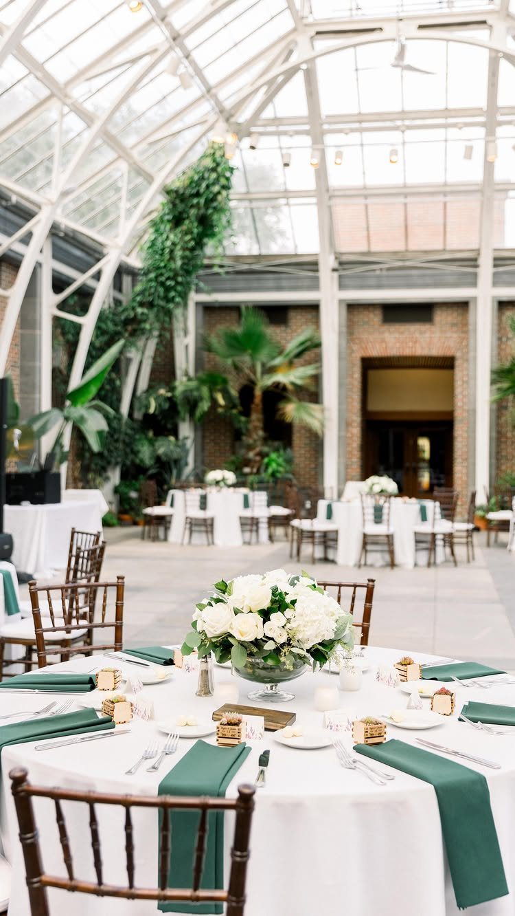 Wedding reception tables with white flowers inside a bright glass botanical conservatory.