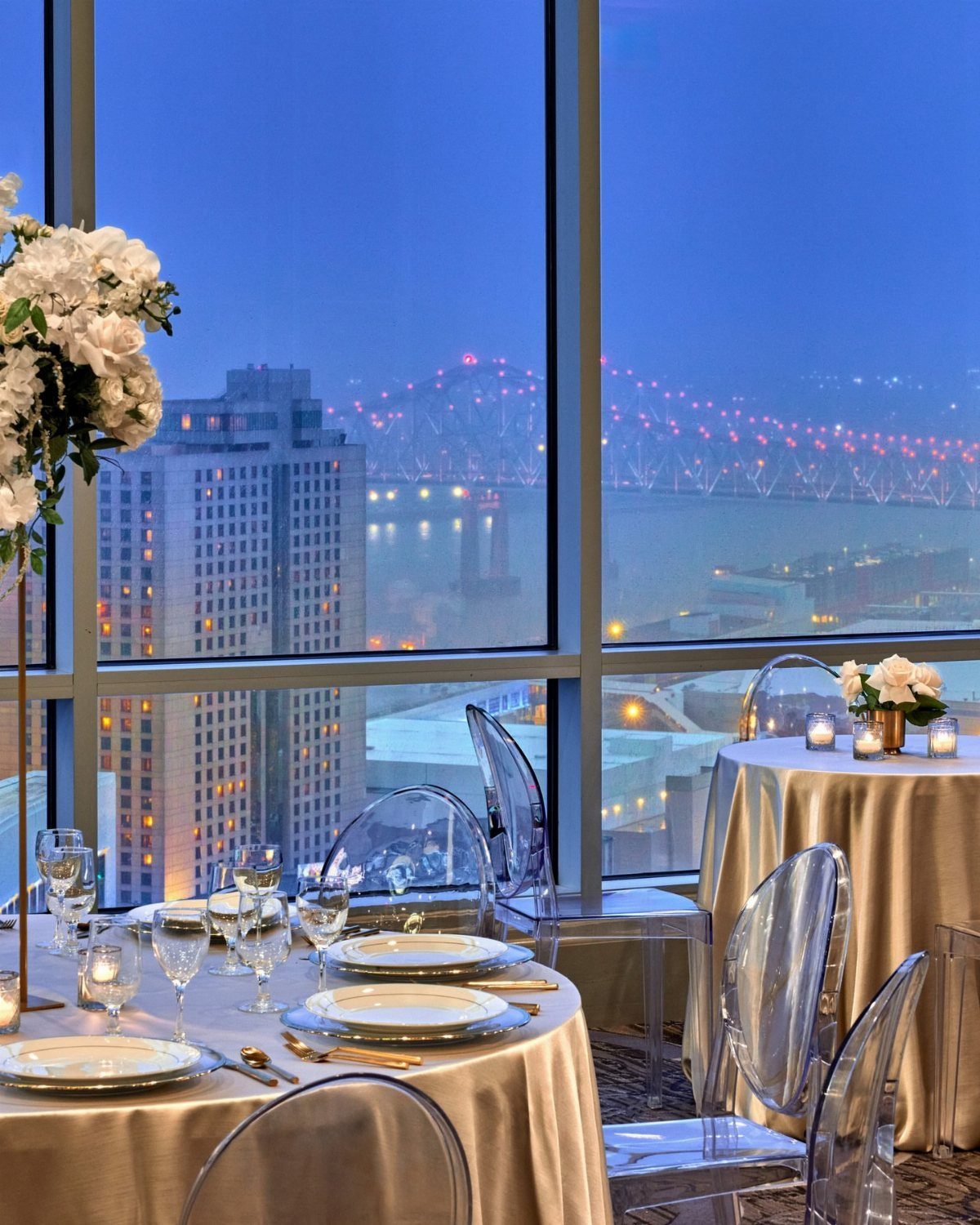 Elegant wedding reception tables with gold linens overlooking a city skyline and bridge.