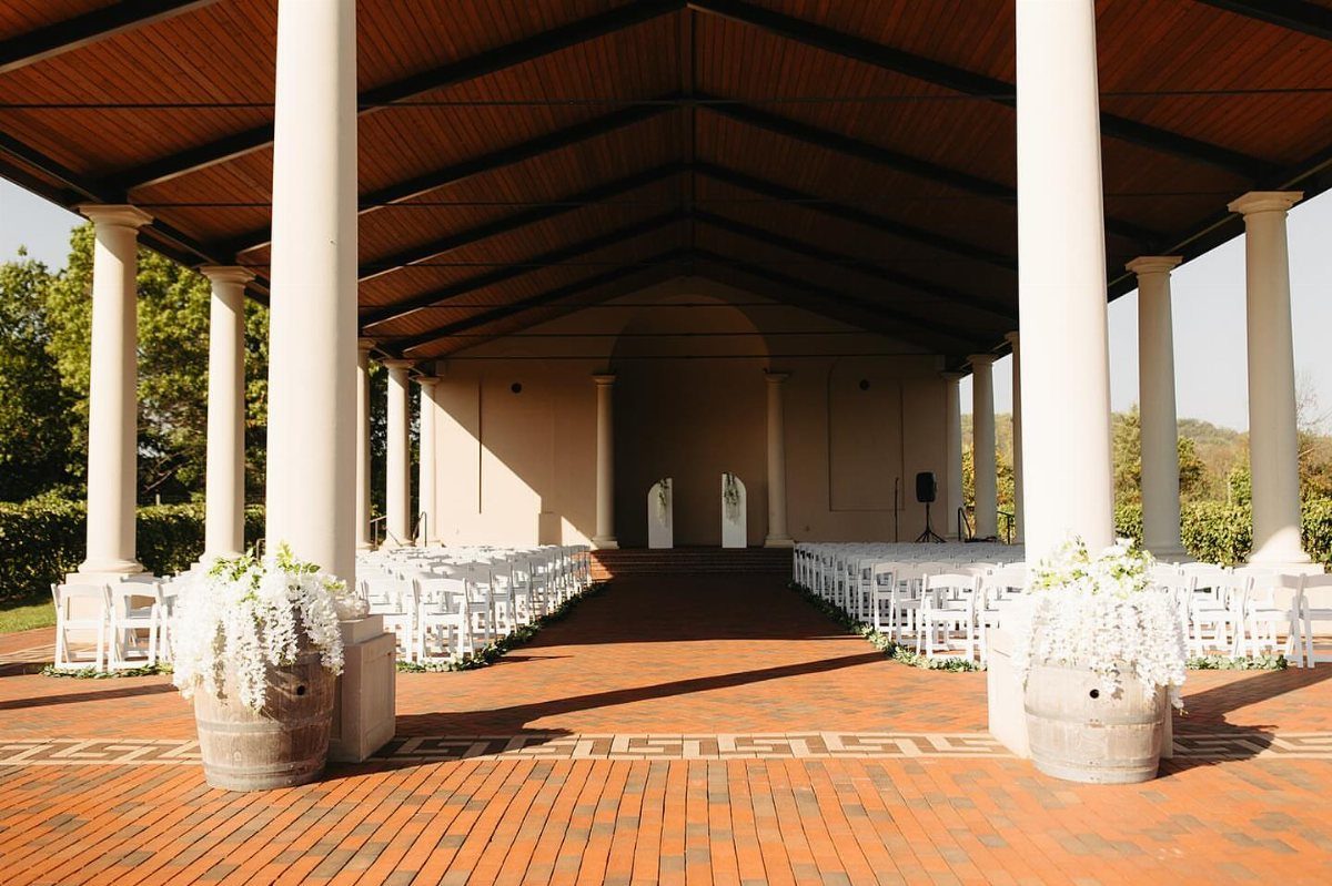 Covered pavilion with white columns and white chairs set up for a wedding ceremony.