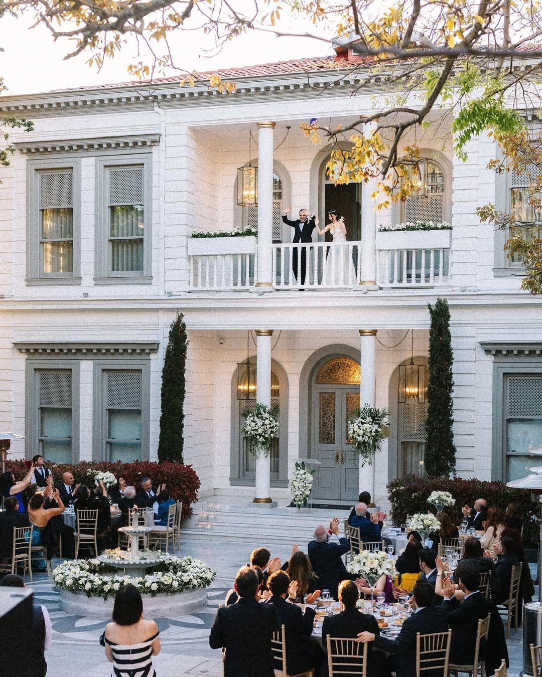 White historic mansion wedding venue with guests dining outdoors and couple on balcony