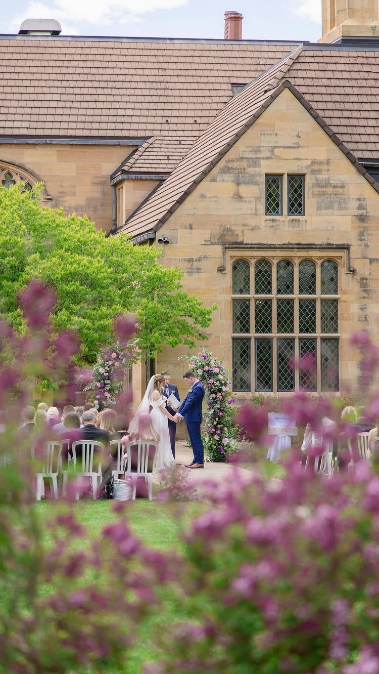Wedding ceremony with a bride and groom before a historic stone building and gardens.