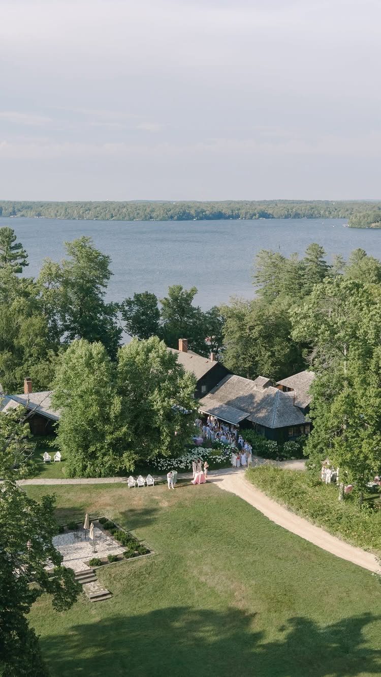 Dark lodge with gabled roof surrounded by trees overlooking a large blue lake.