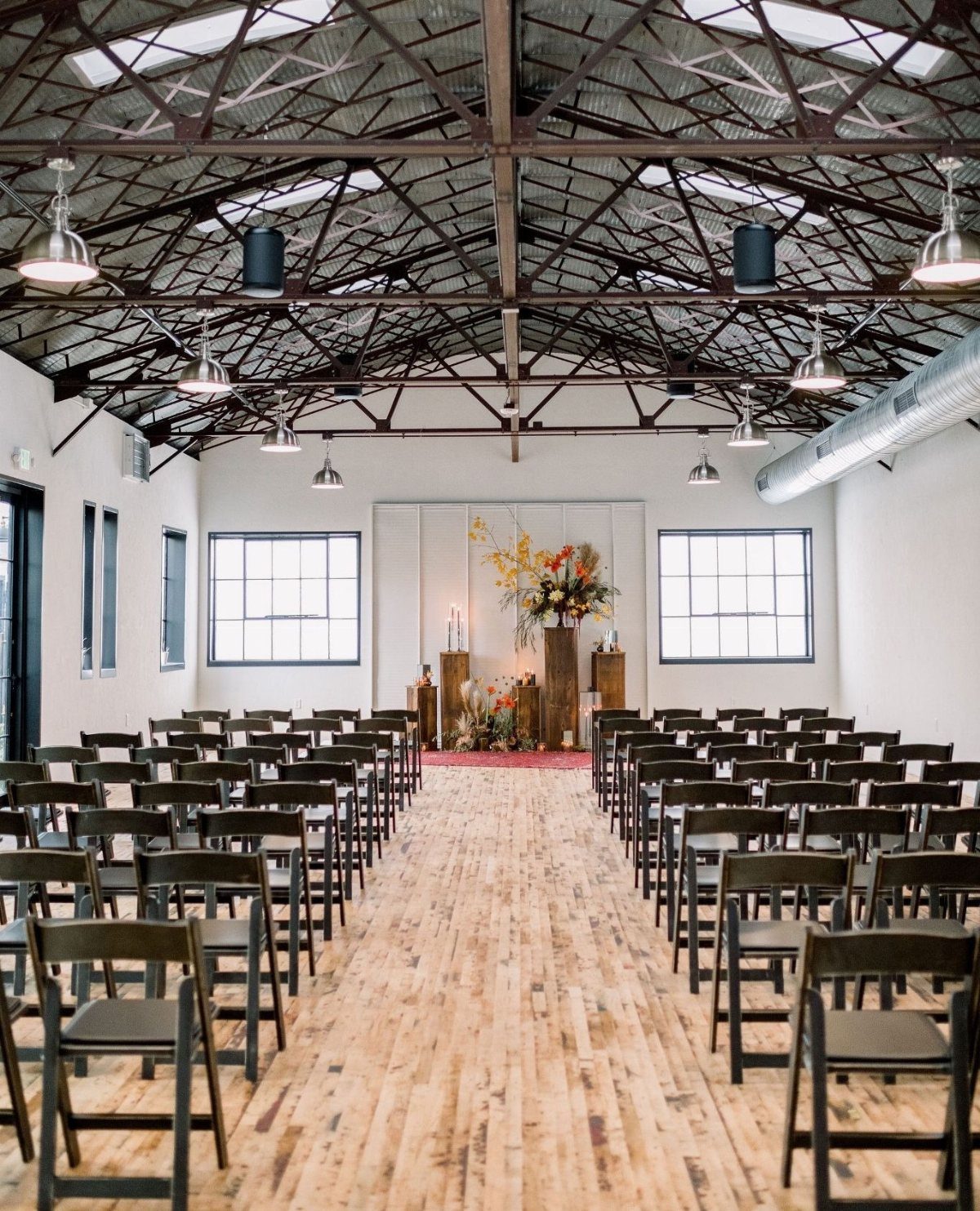 Industrial wedding ceremony space with black chairs, wooden floors, and exposed metal ceiling.