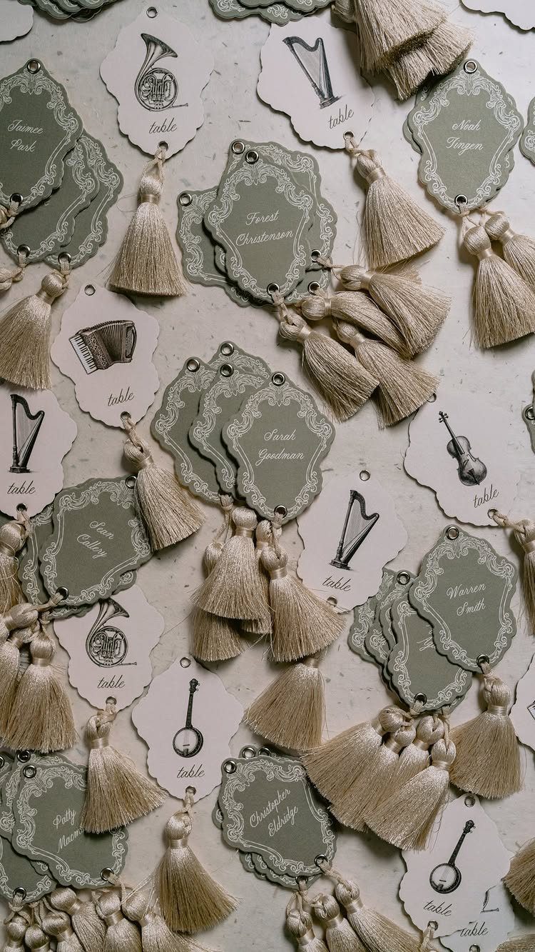 Ornate sage green and white escort cards with musical illustrations and beige tassels.