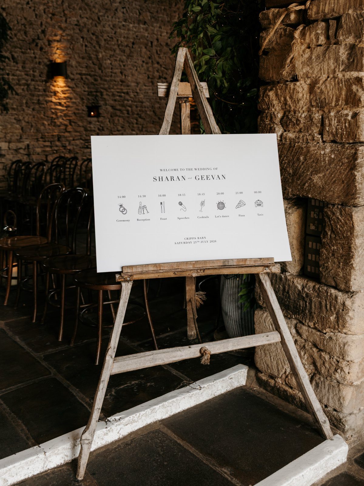 White event itinerary sign on a rustic wooden easel against a stone wall.