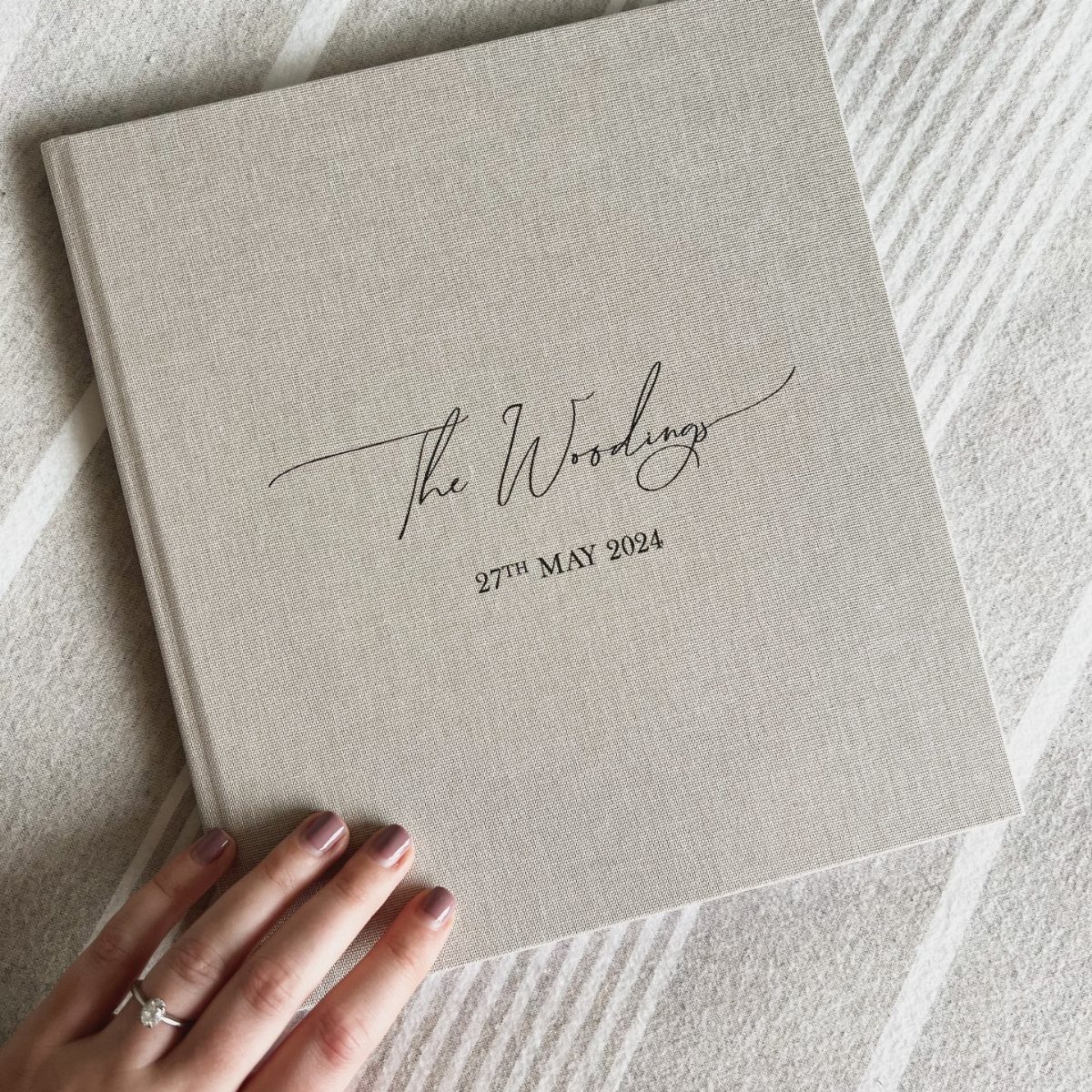 Beige linen guest book with personalized wedding names and date on a striped surface