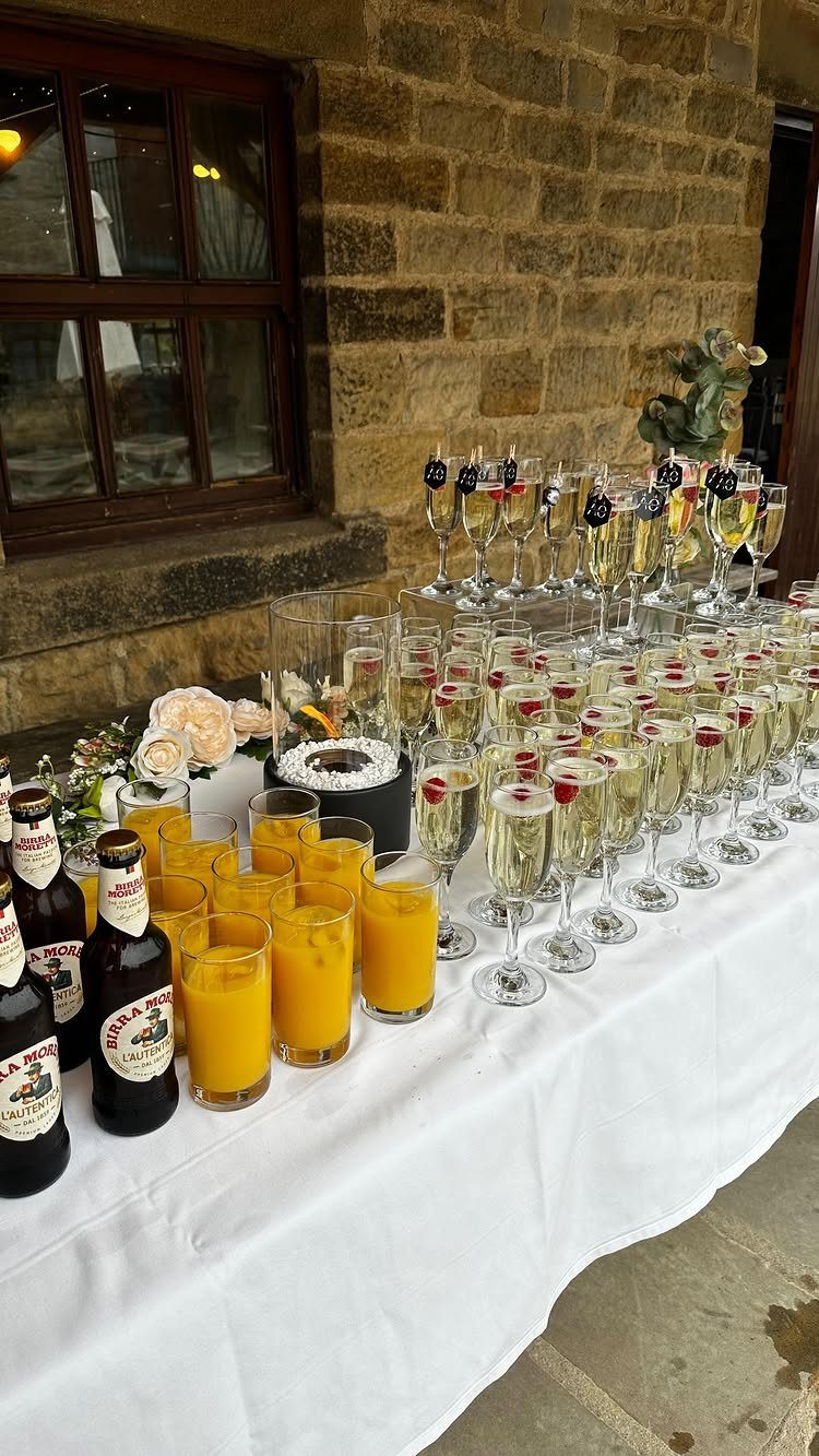Assorted champagne flutes and orange juice glasses arranged on a white tablecloth.