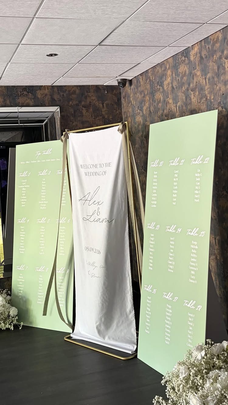 White fabric welcome sign on gold frame with green seating chart panels