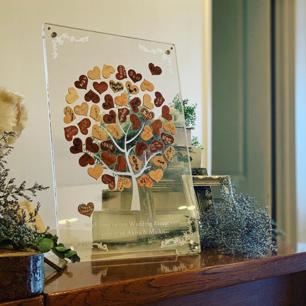 Acrylic wish tree plaque with heart-shaped wooden tags on a wedding welcome table.